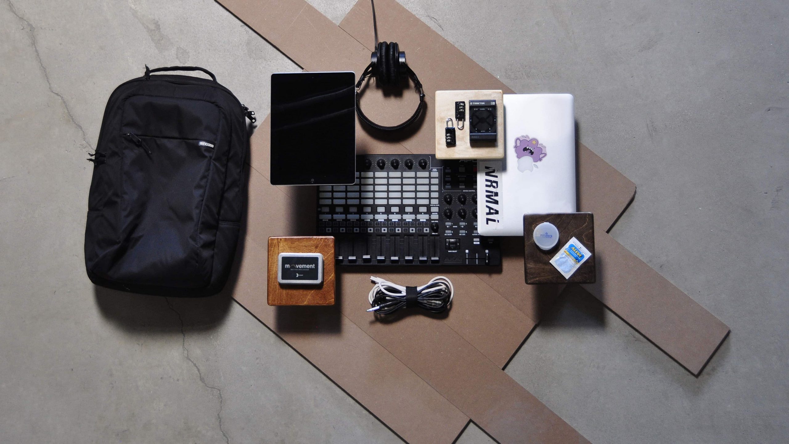 Travel essentials for musicians including an iPad, laptop, cables, headphones, suitcase locks, a MIDI controller, and external storage