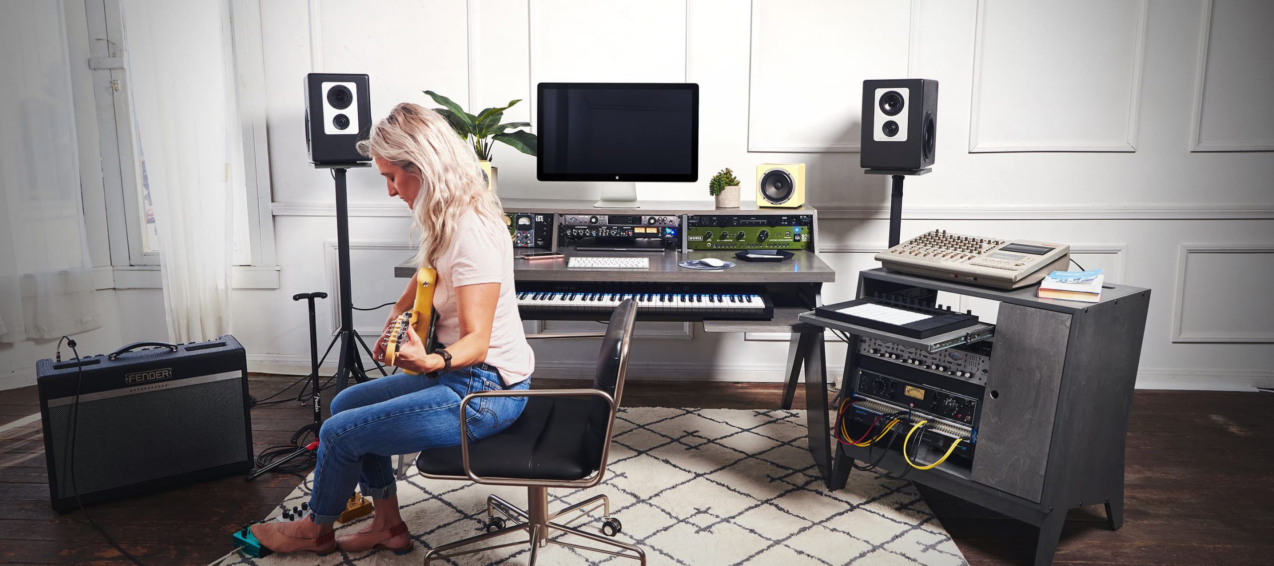 Woman in studio playing guitar with grey Output Platform desk and grey Output Sidecar accessory.
